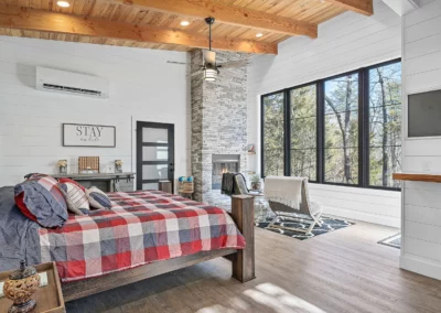 A large room with a large bed, stone fireplace, and large viewing windows sit clean and bright at Whispering Pines cabin.