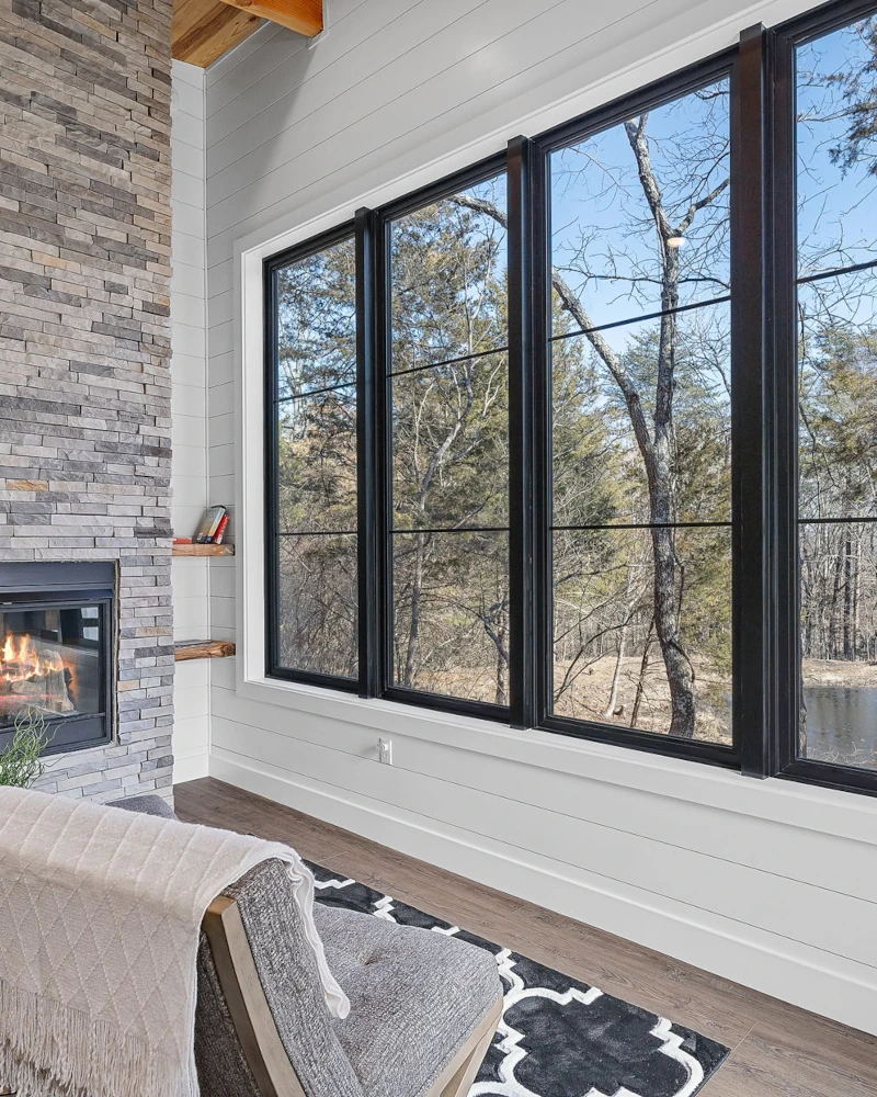 A comfortable chair looks out through large windows to nature at Whispering Pines cabin.