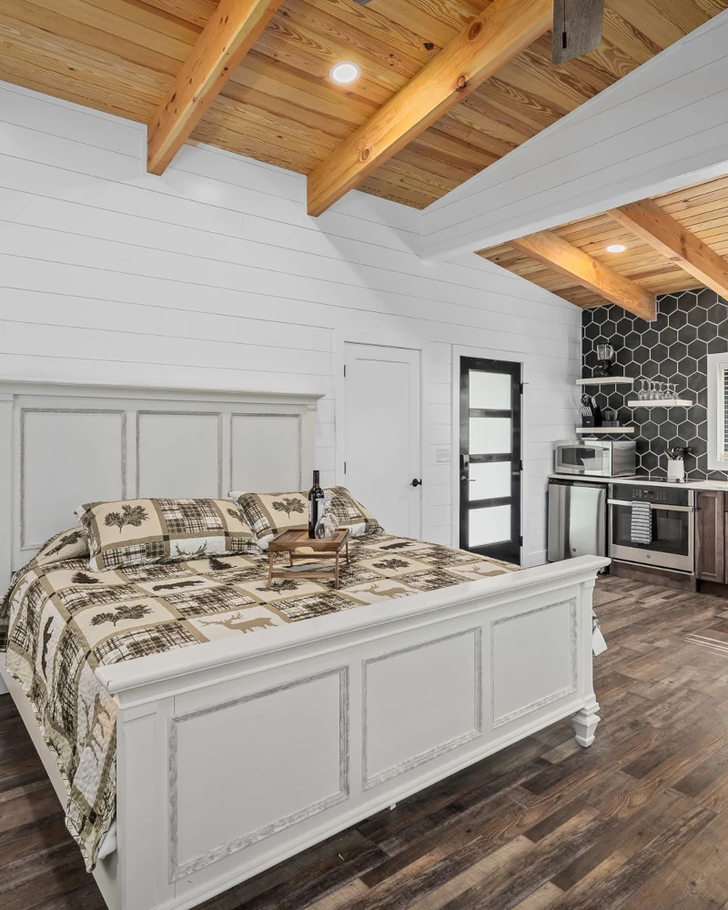 Whispering Pines - Twilight - Open Concept A luxurious king size bed with fluffy pillows and bed sheets in a room with high walls looking out to a forest.