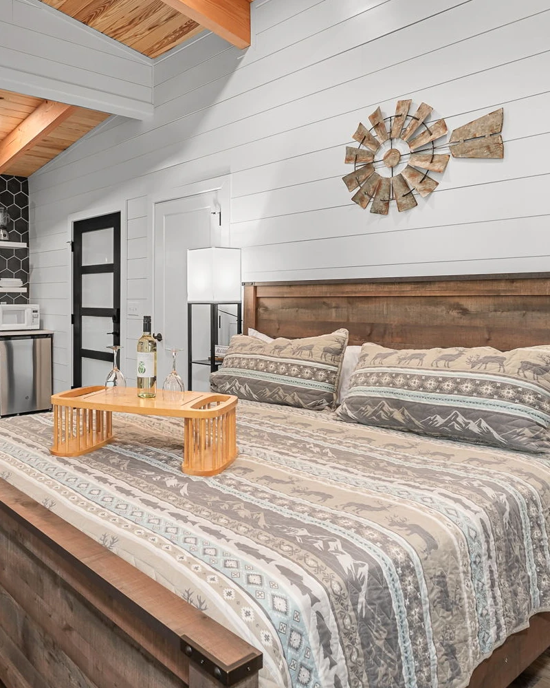 A luxurious king size bed with fluffy pillows and bed sheets in a room with high walls looking out to a forest.
